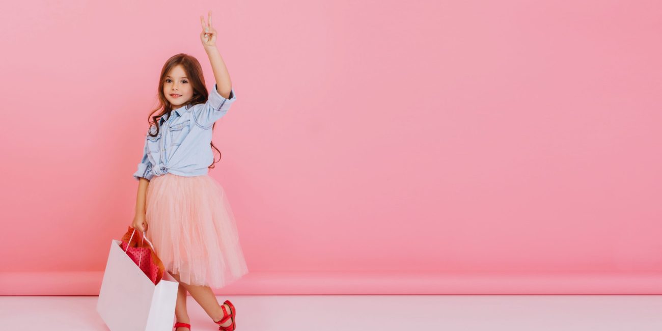 Pretty little girl in tulle skirt with package with present walking isolated on pink background, smiling to camera. Cute friendly child expressing true positive emotions. Place for text